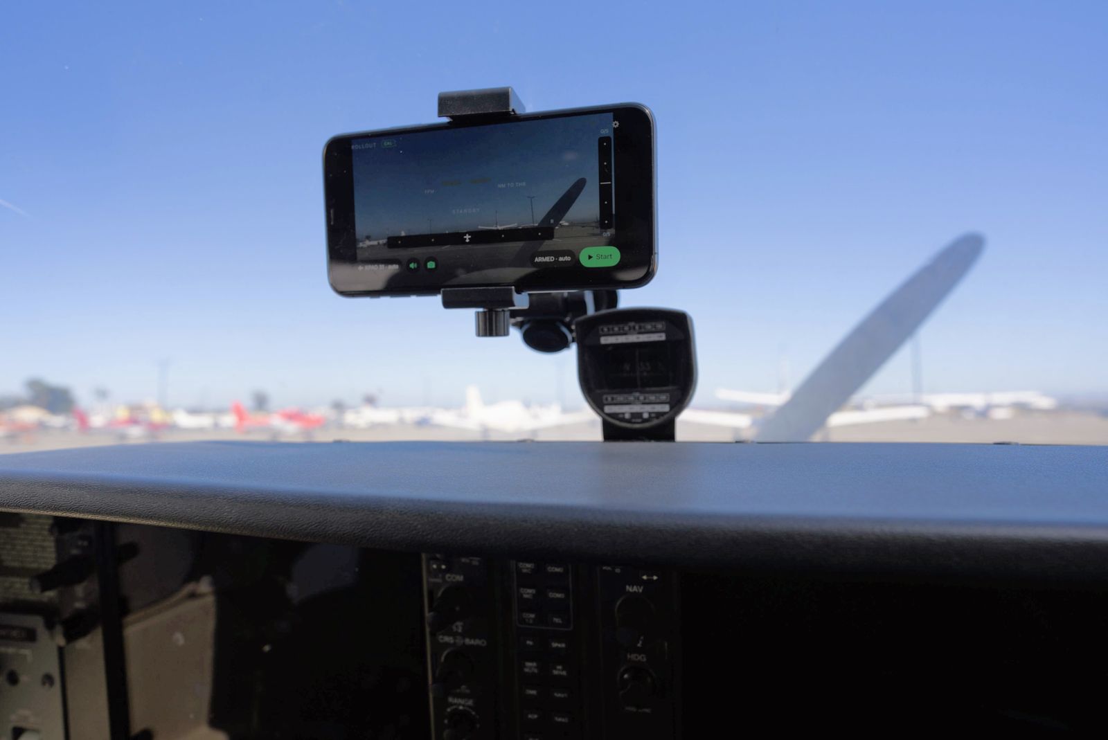 An iPhone held in landscape by a suction mount at the base of the windshield, above
             the glareshield, with its rear camera looking forward down the ramp. The screen shows
             the GonnaLand home screen armed for KPAO runway 31, with the propeller and parked
             aircraft visible through the windshield beyond it.